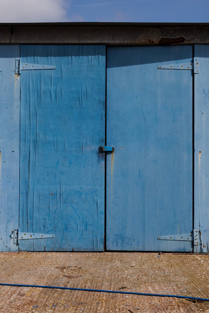 Rustic blue wooden garage door with metal hinges on barn exterior.