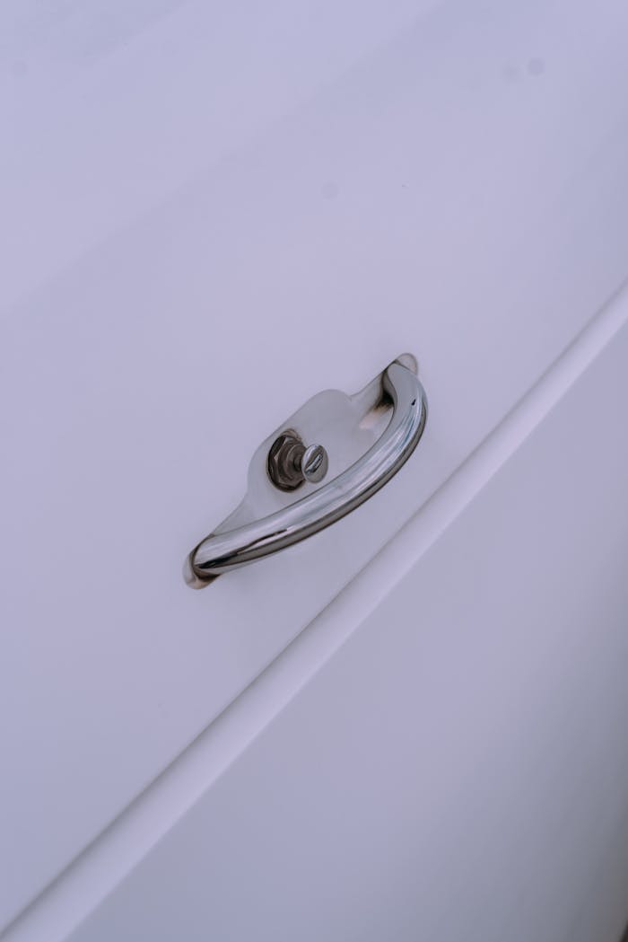 Close-up image of a chrome handle on a white cabinet door, emphasizing sleek design and minimalism.
